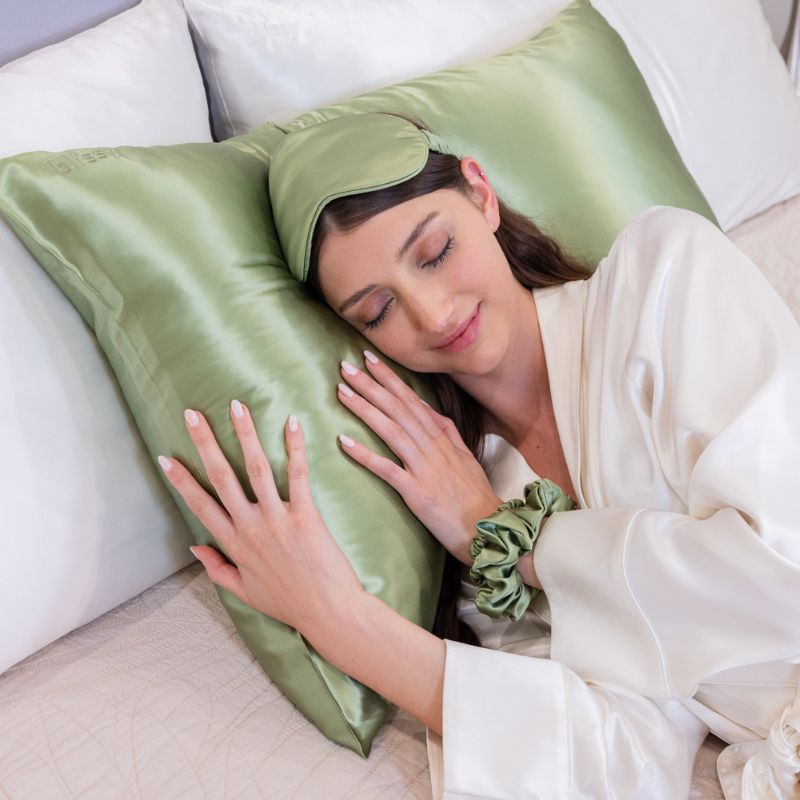 Woman resting on a green Blissy silk pillowcase and sleep mask, showcasing the luxury behind the world's best silk pillowcase brand